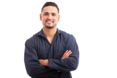 Smiling man in a blue shirt with arms crossed in front of a white background.